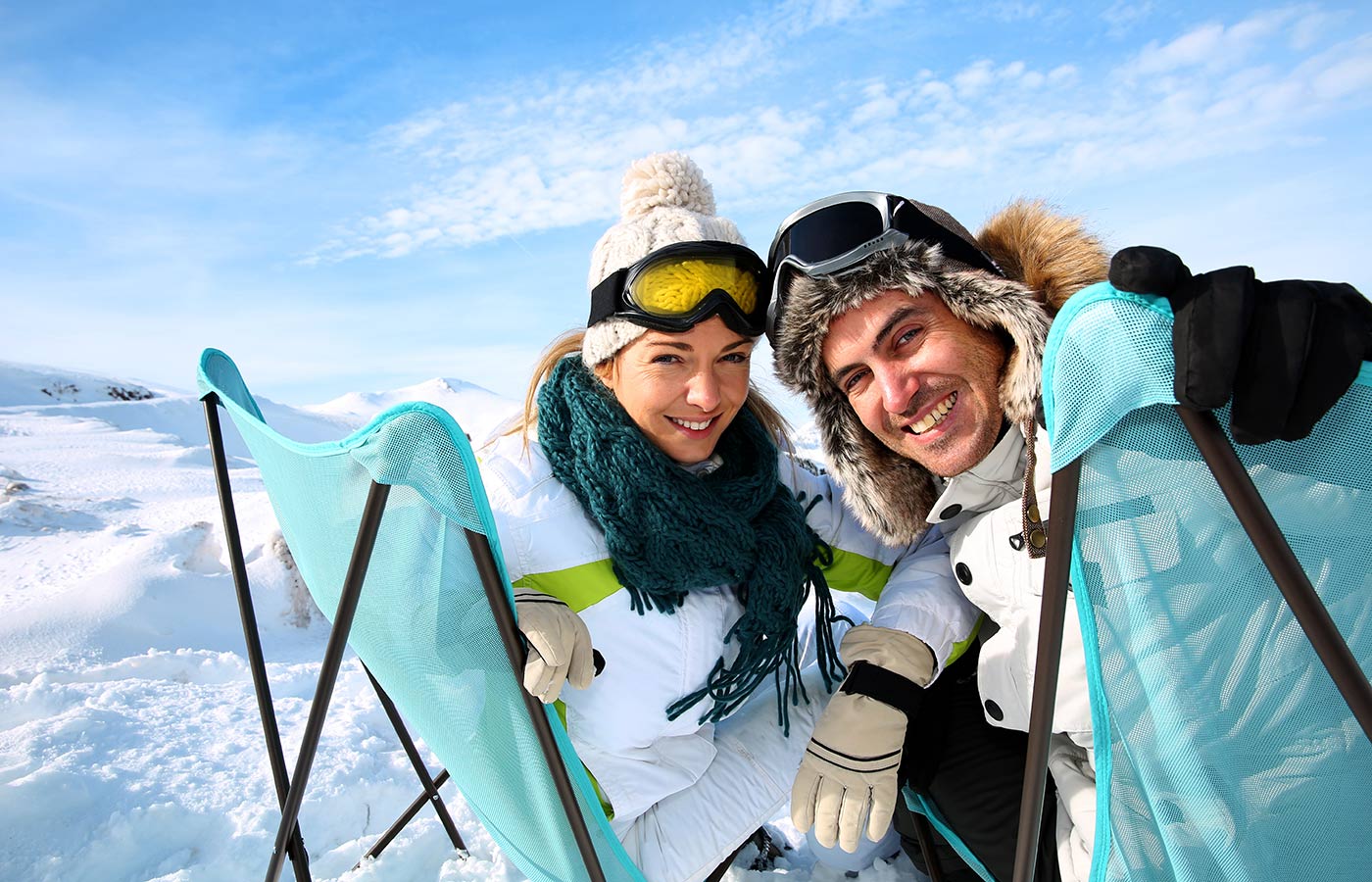 Giovane coppia sorridente vestita da neve si gode il sole di montagna su delle sdraio sulla neve