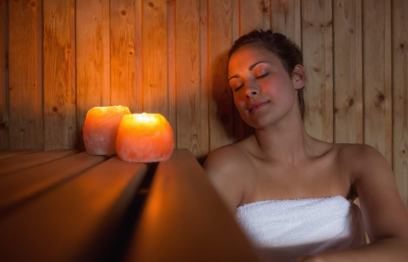 Frau in der Sauna entspannt sich mit geschlossenen Augen, bei Kerzenlicht.