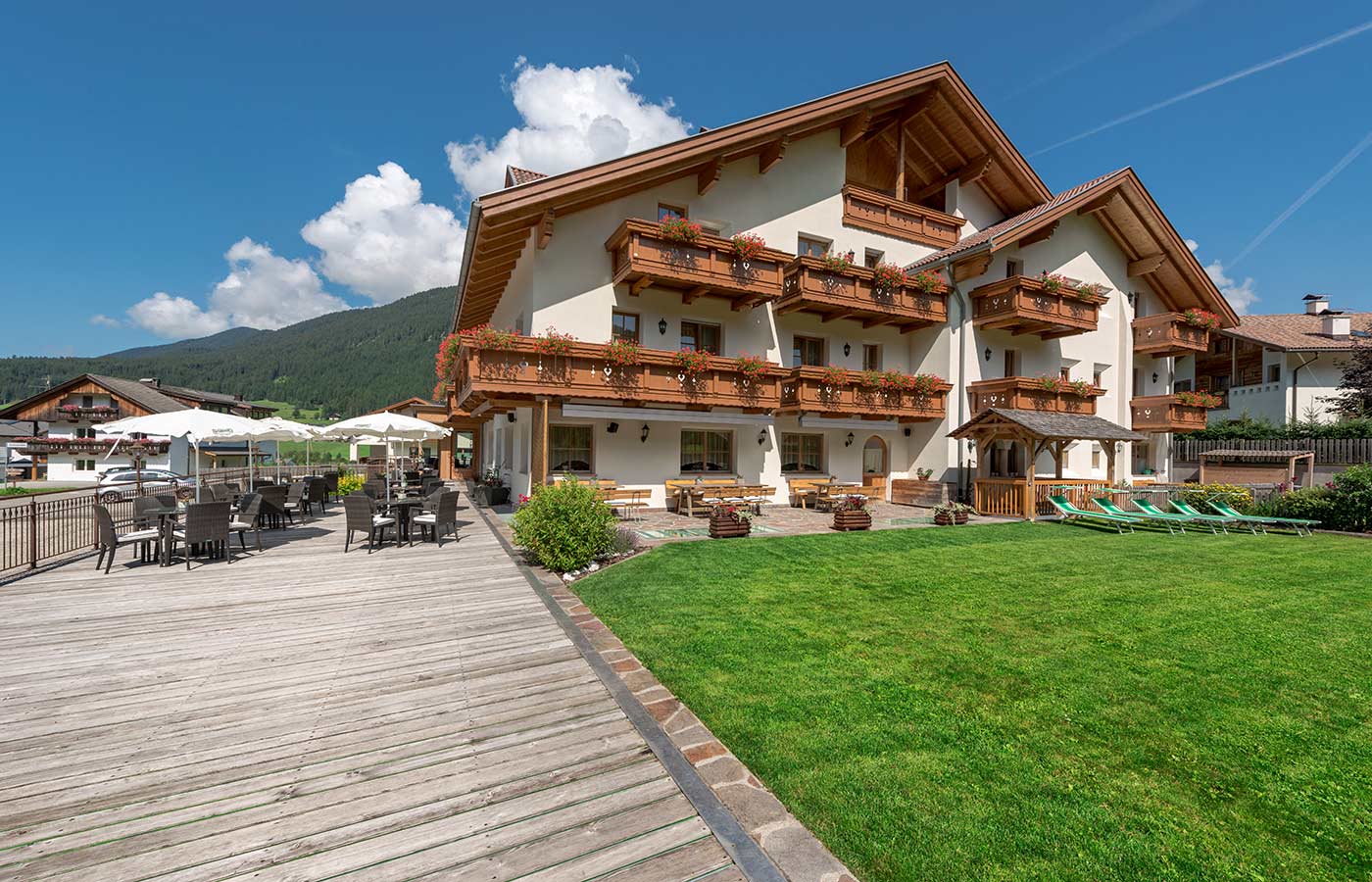 veduta esterna dell'Hotel Waldheim in Val Casies con giardino e veranda con tavolini in una giornata d'estate