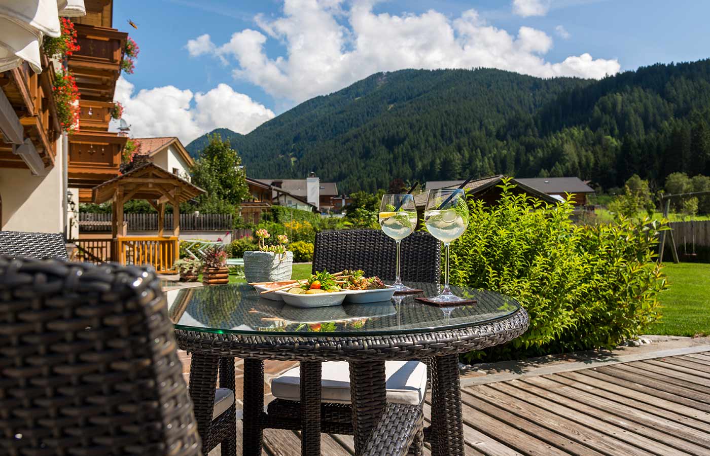 tavolino nel giardino dell'Hotel Waldheim in Alto Adige preparato con due bicchieri di vino e stuzzichini per l'aperitivo