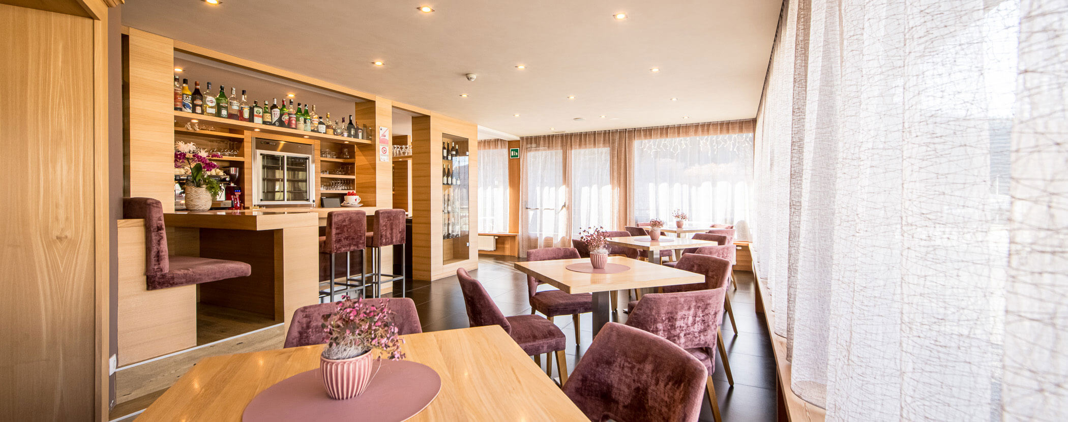 Modernes Café mit Holzdekor, lilafarbenen Stühlen und großen Fenstern, die natürliches Licht hereinlassen. - Hotel Waldheim