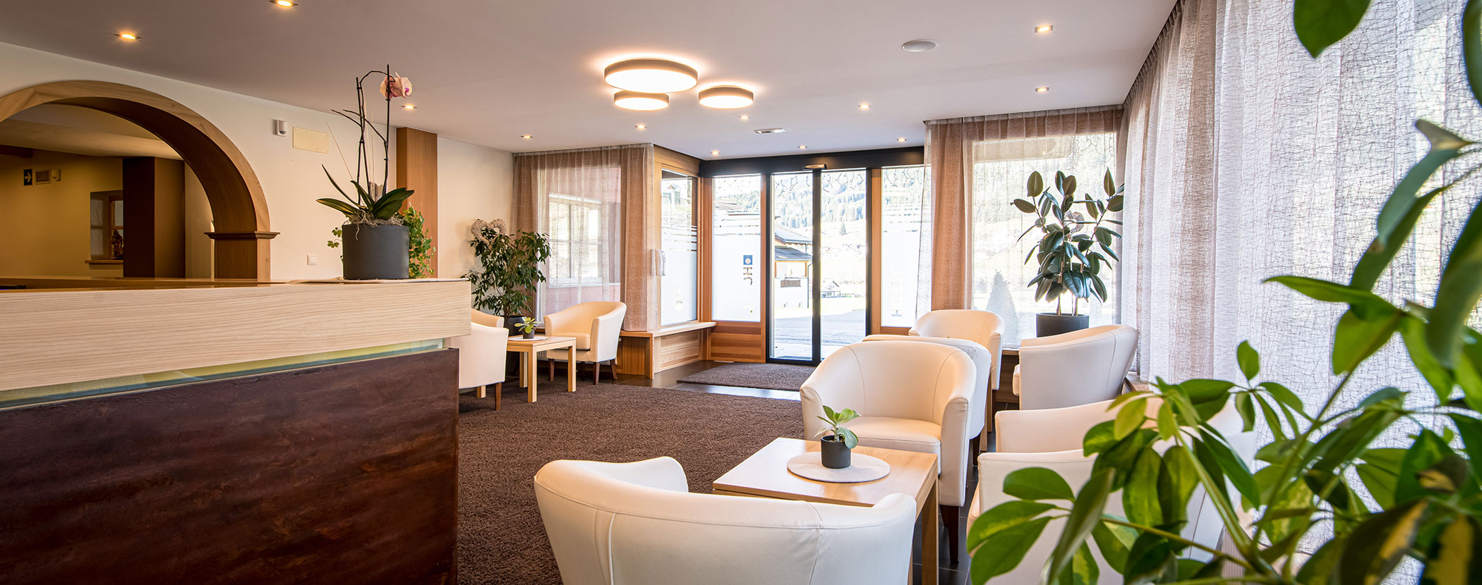 Helles, modernes Wartezimmer mit weißen Stühlen, Topfpflanzen und großen Fenstern, die natürliches Licht hereinlassen. - Hotel Waldheim