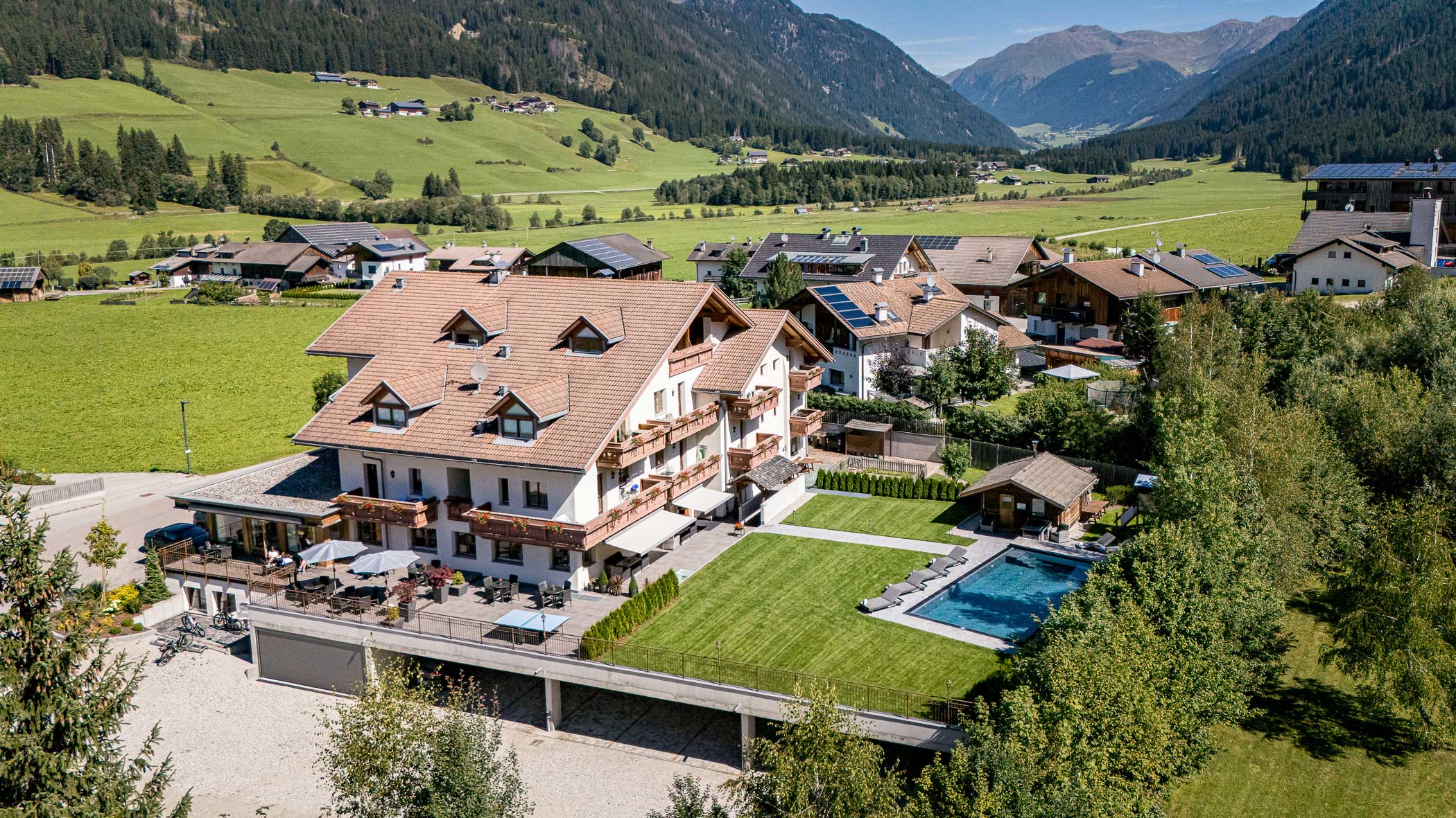 Ein großes Haus im Chalet-Stil mit Pool, Rasen und Bergblick in einem grünen Tal mit verstreuten Häusern. - Hotel Waldheim