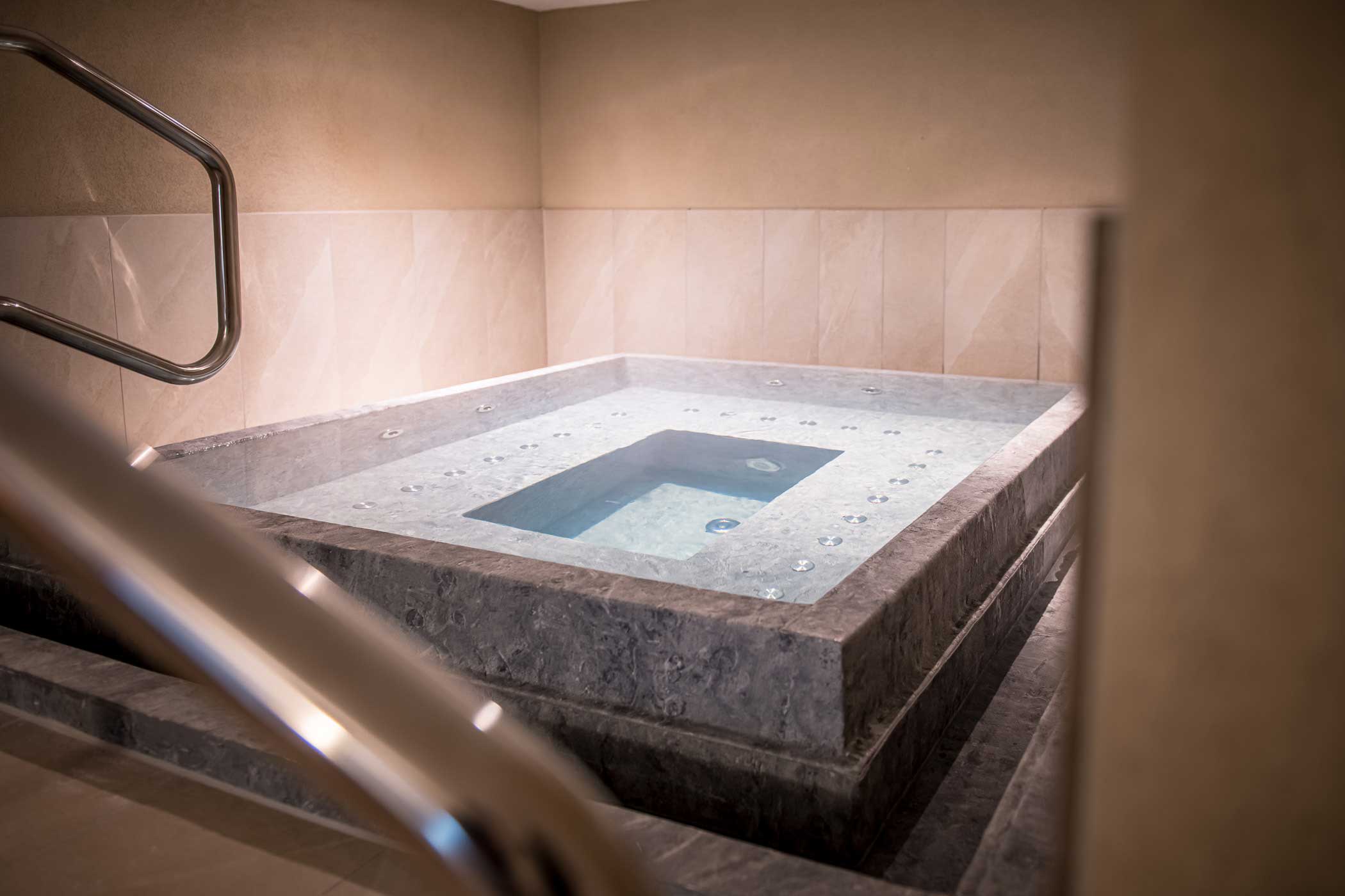 Innenwhirlpool mit Marmorkanten, Düsen und Metallgeländer in einem sanft beleuchteten Spa-Raum. - Hotel Waldheim