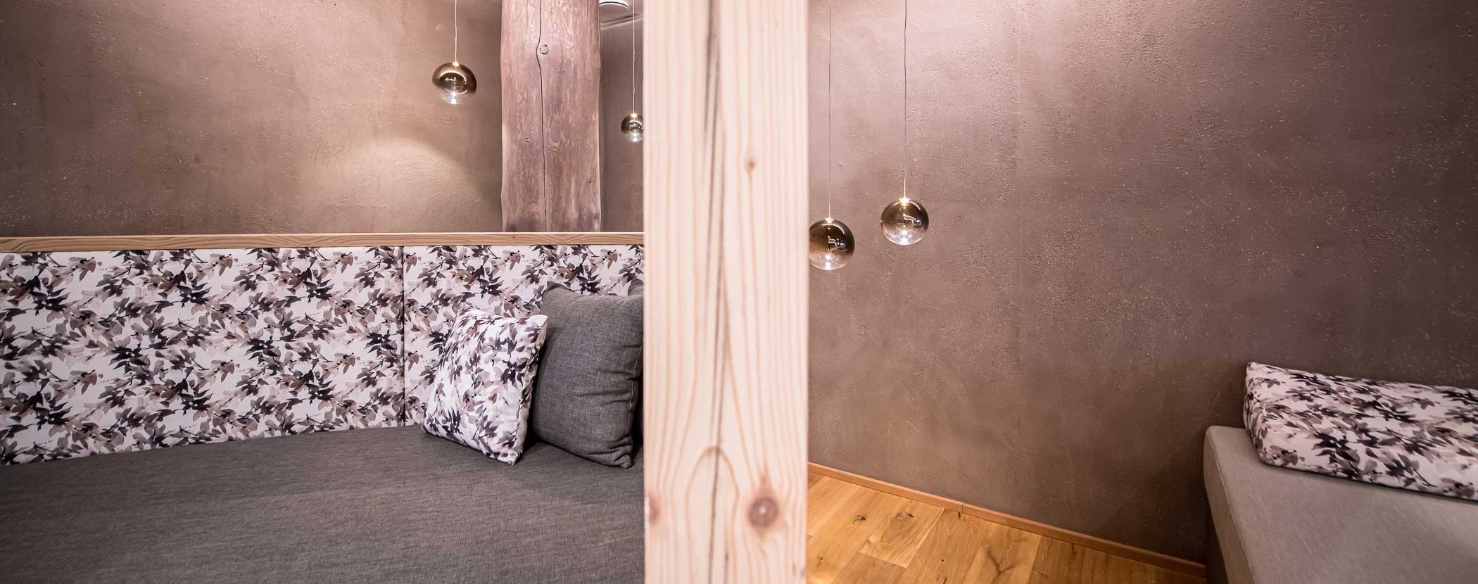Gemütliches Zimmer mit blumengemustertem Sofa, grauen Kissen, Holztrennwand und Hängelampen. - Hotel Waldheim