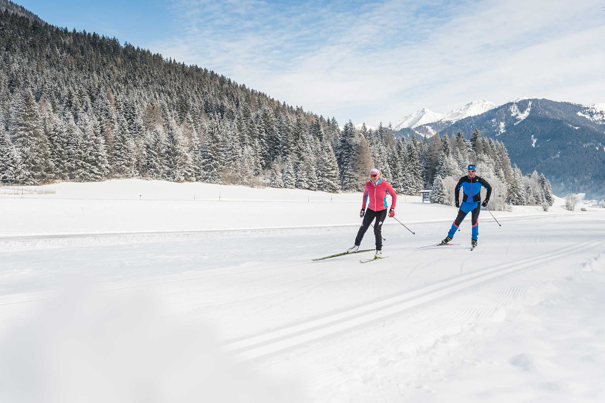 Zwei Personen beim Skilanglauf auf einer verschneiten Loipe mit bewaldeten Bergen im Hintergrund. - Hotel Waldheim