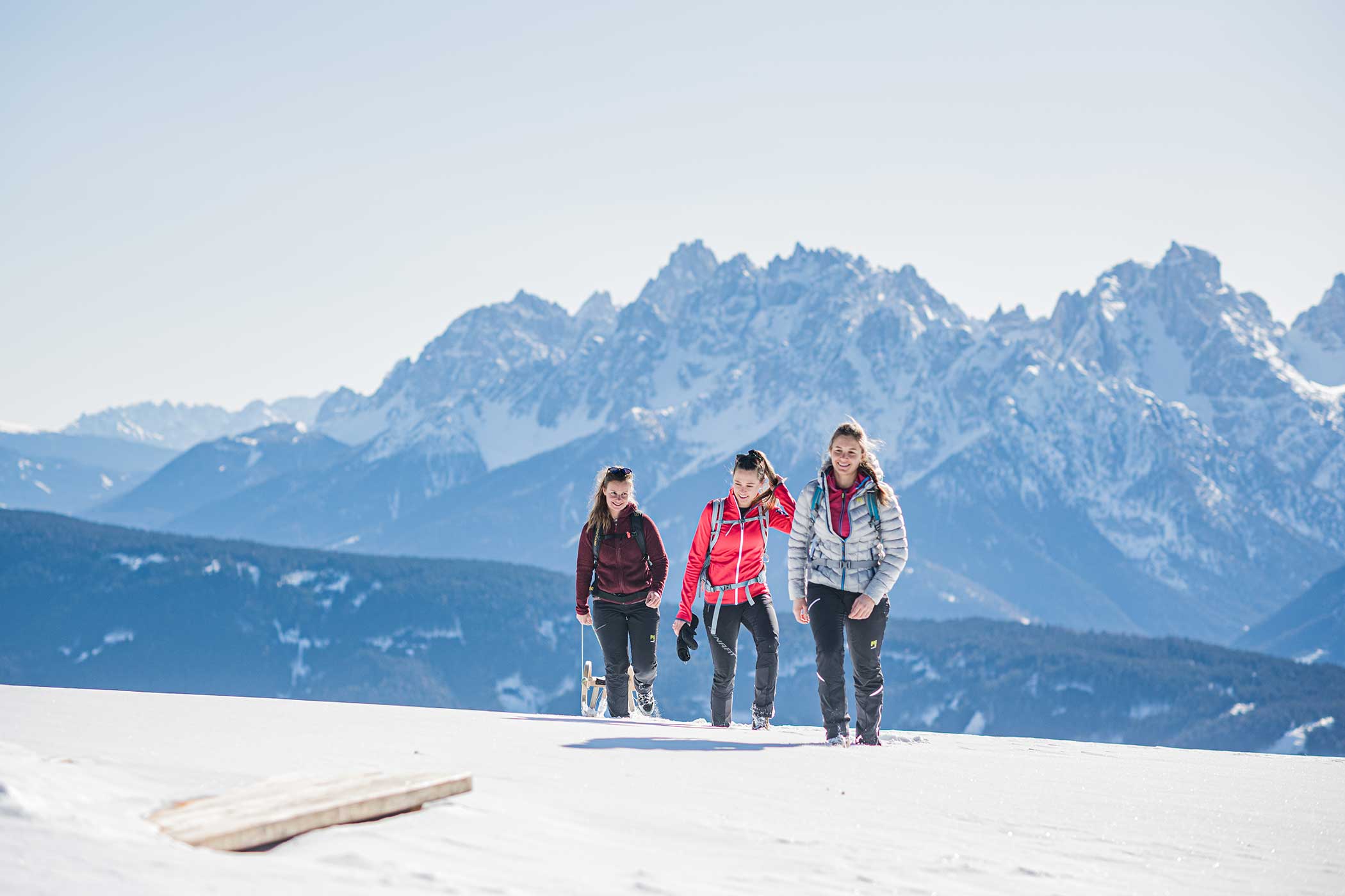 Drei Personen wandern im Schnee mit schneebedeckten Bergen im Hintergrund unter einem klaren blauen Himmel. - Hotel Waldheim