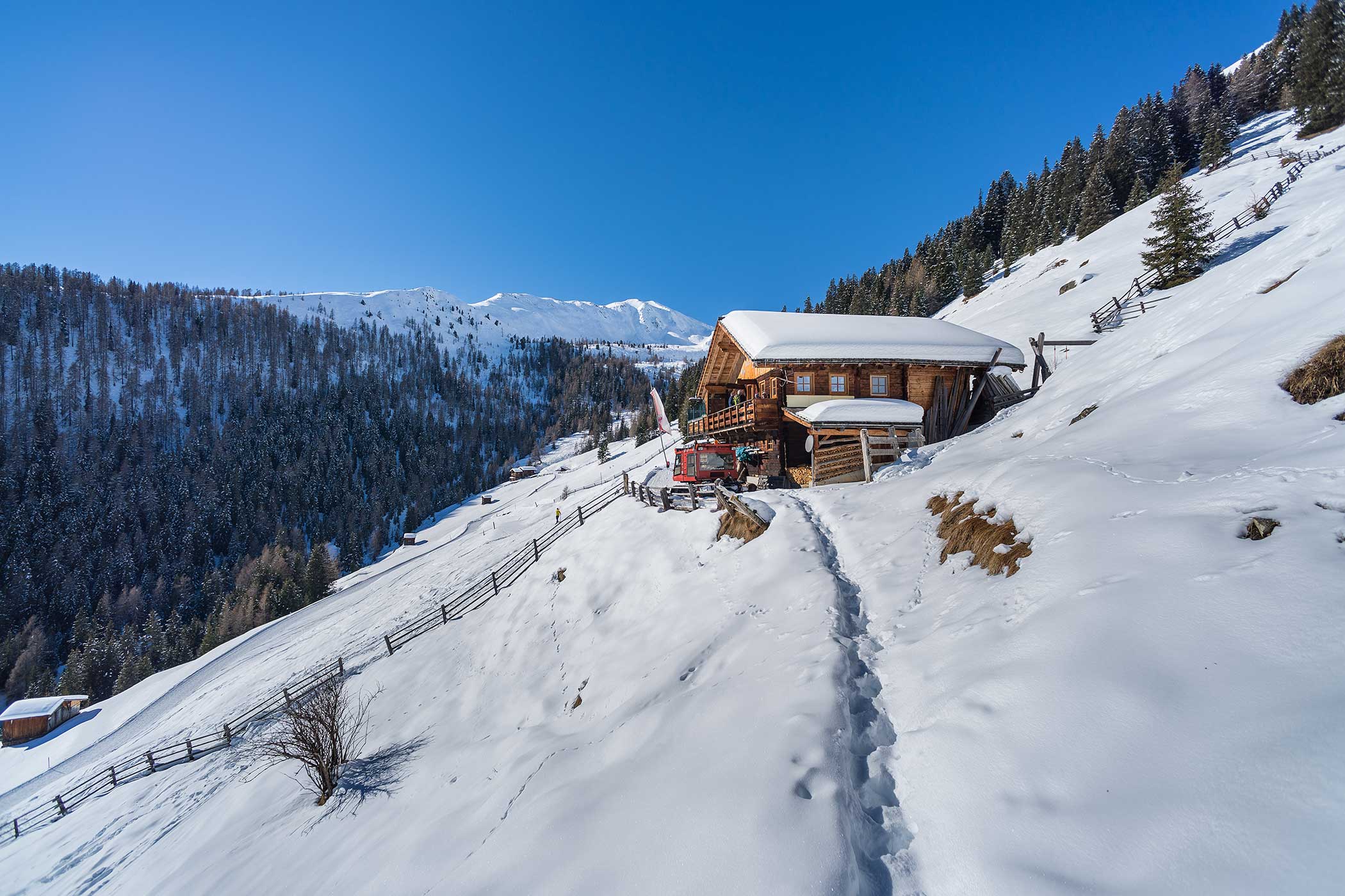 Eine verschneite Berghütte mit einem Holzzaun und Bäumen unter einem strahlend blauen Himmel. - Hotel Waldheim