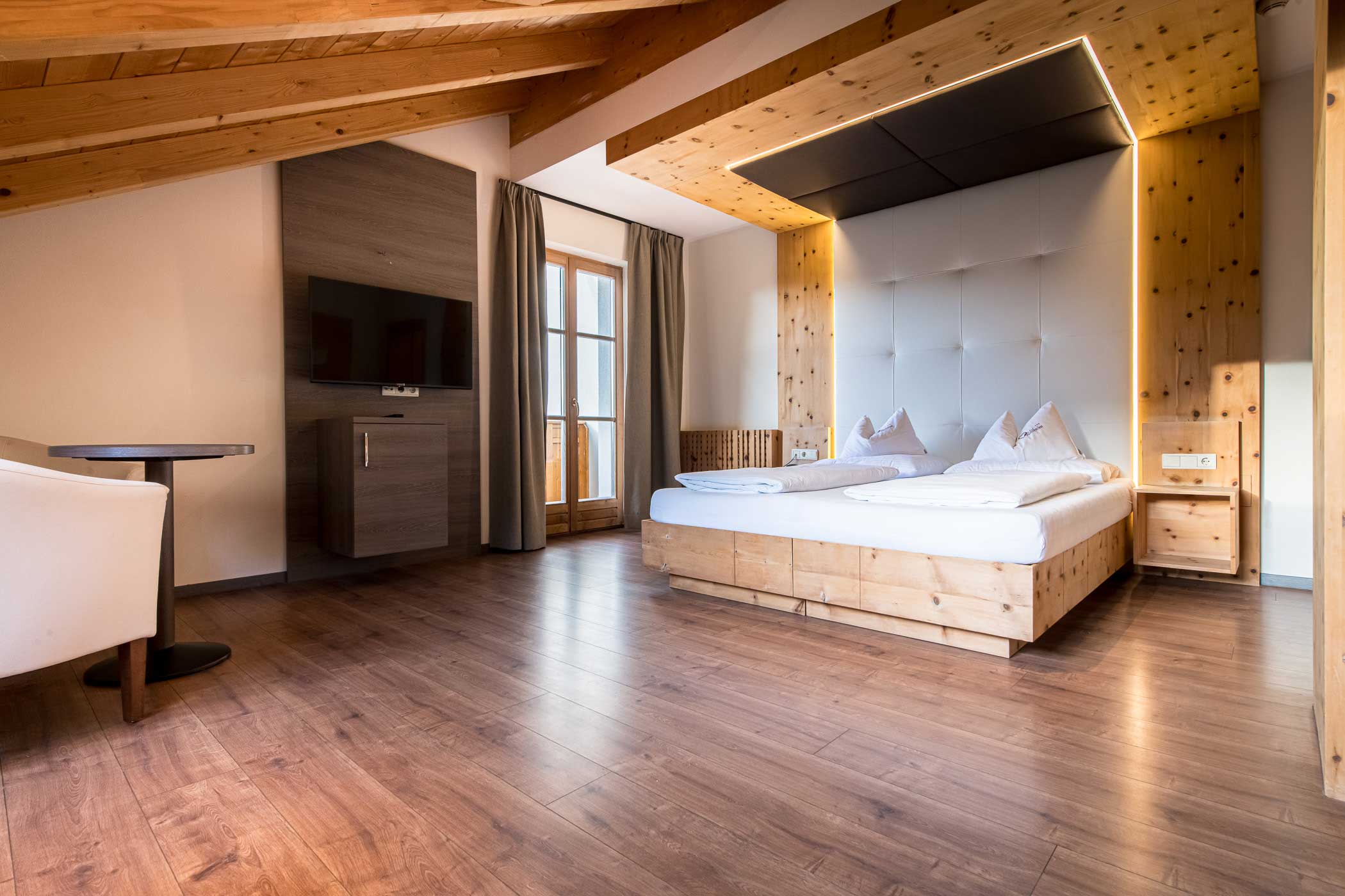 Modernes Hotelzimmer mit Holzfußboden, großem Bett, TV, Schreibtisch und einem Fenster mit Vorhängen. - Hotel Waldheim