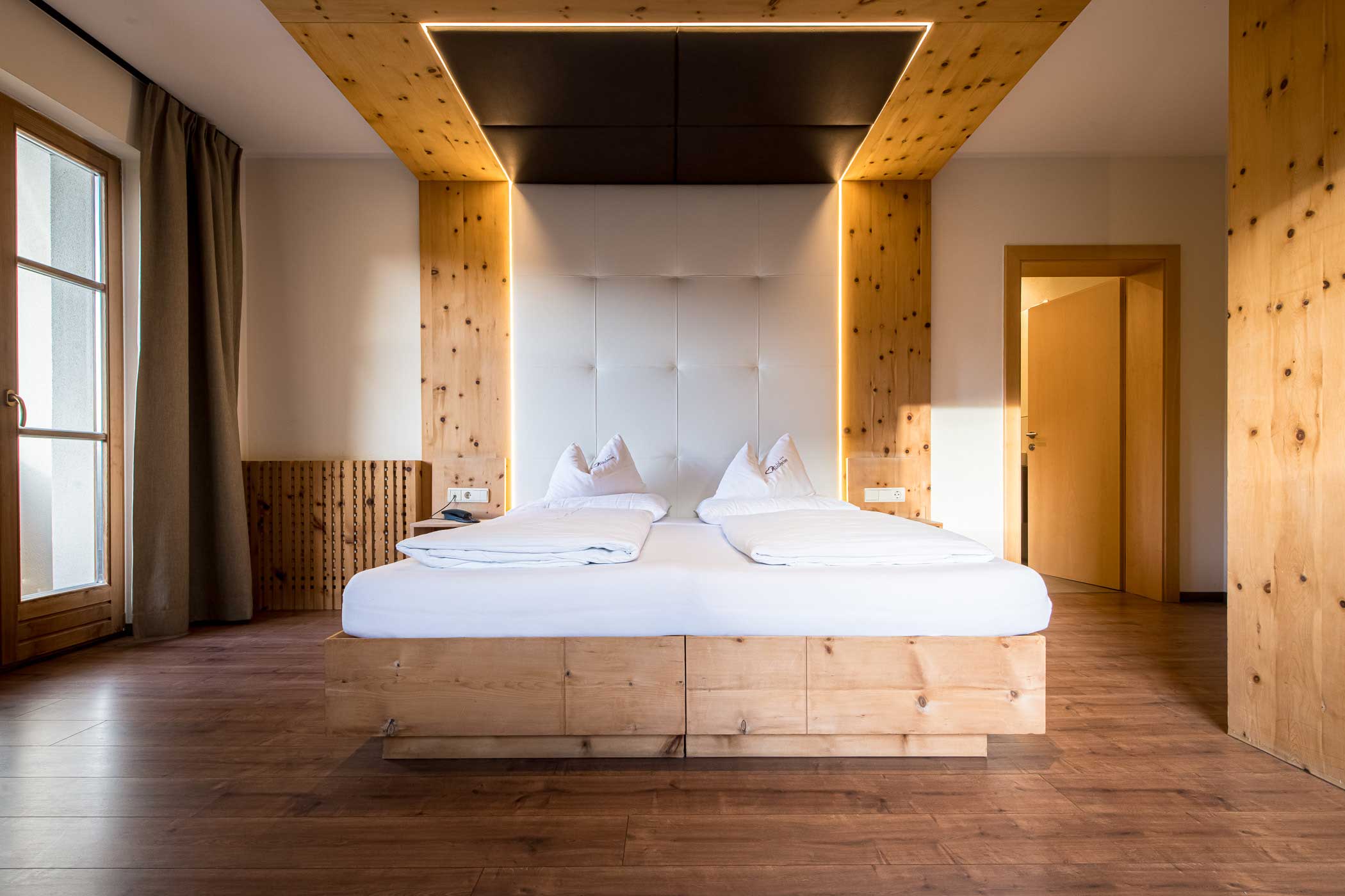 Modernes Hotelzimmer mit Holzakzenten, einem Doppelbett und warmem Tageslicht durch ein Fenster auf der linken Seite. - Hotel Waldheim