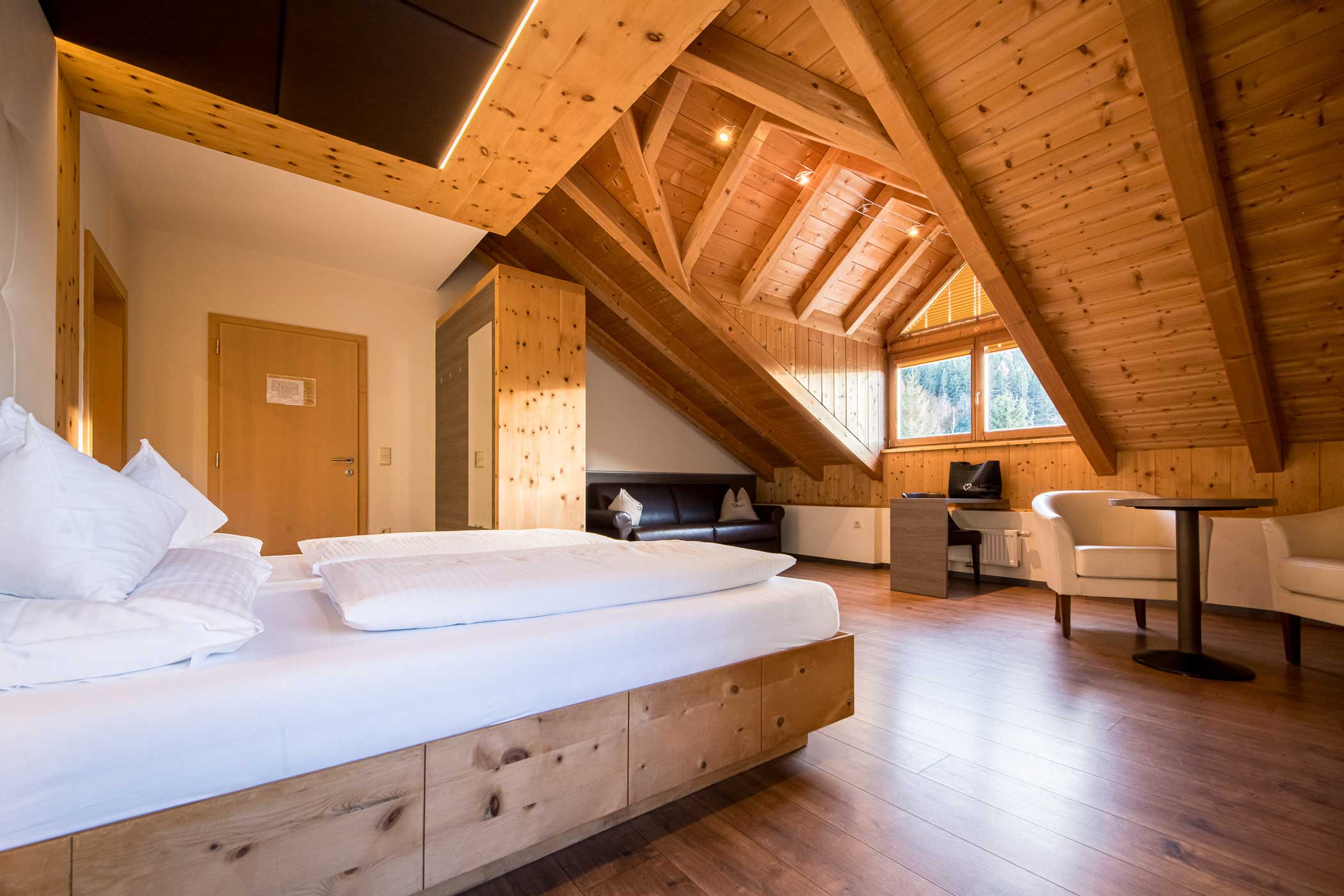 Gemütliches Hotelzimmer im Dachgeschoss mit schräger Holzdecke, Doppelbett, Sitzecke und warmem Tageslicht. - Hotel Waldheim